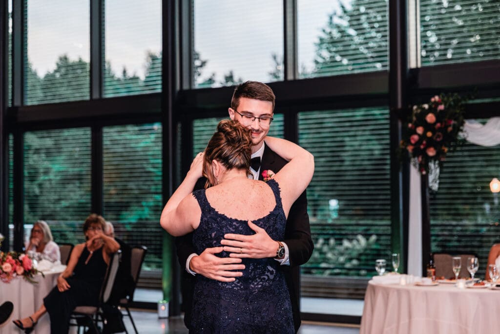 Groom dancing with his mother during wedding reception in front of large garden-view windows at the National Aviary