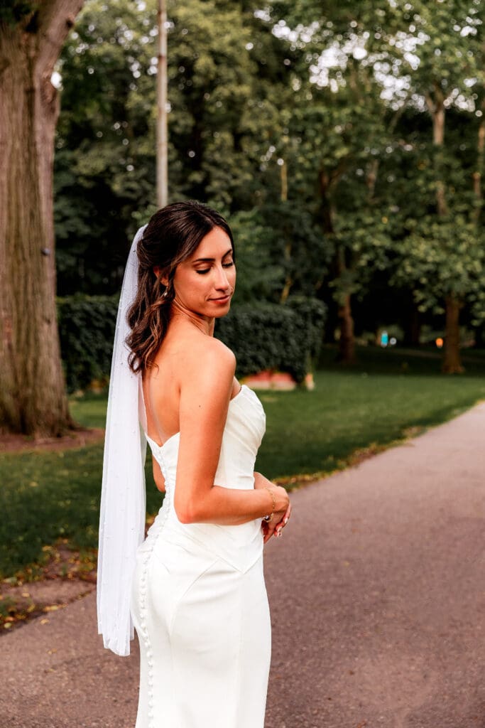 Bride posing in sleek white wedding dress on tree-lined path at sunset near the National Aviary