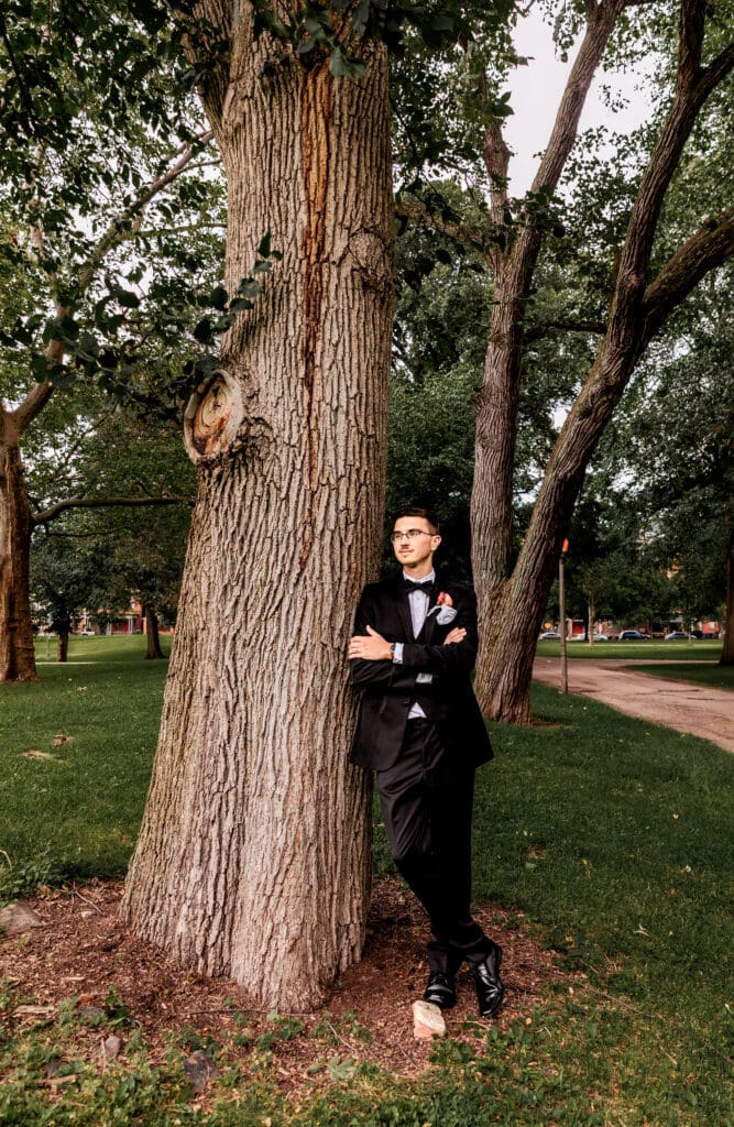 Groom leaning against tree during wedding portraits near the National Aviary at Allegheny Commons Park