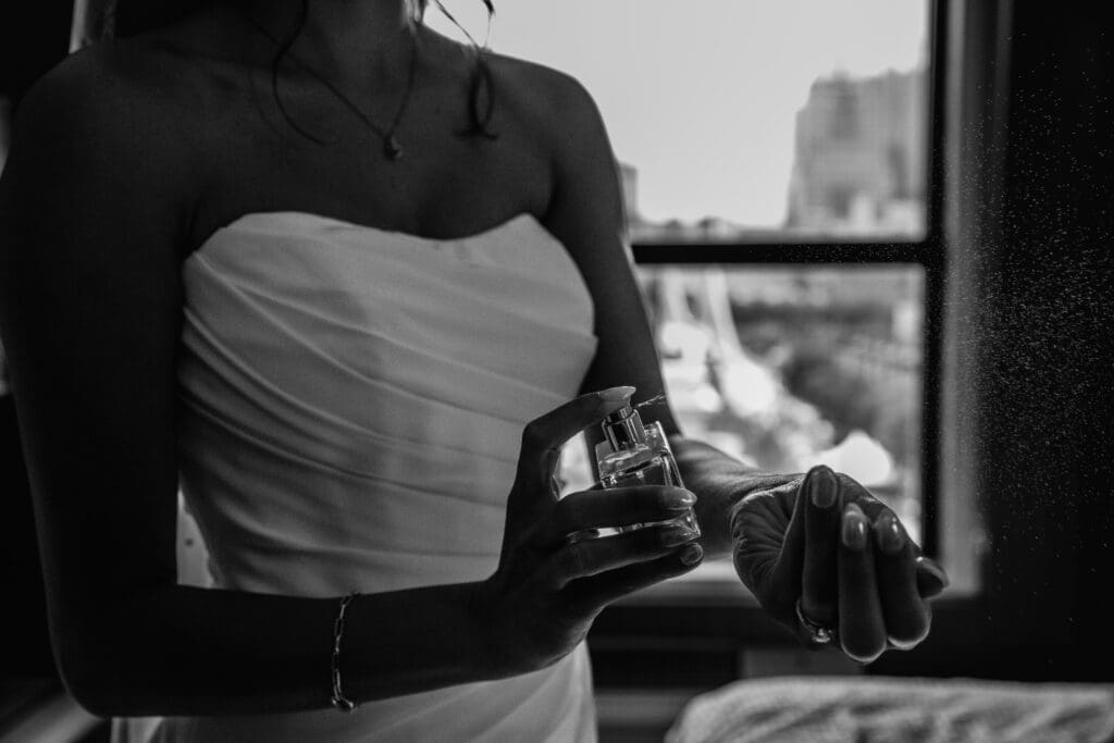 Black and white photo of bride spraying perfume during wedding preparation at the National Aviary