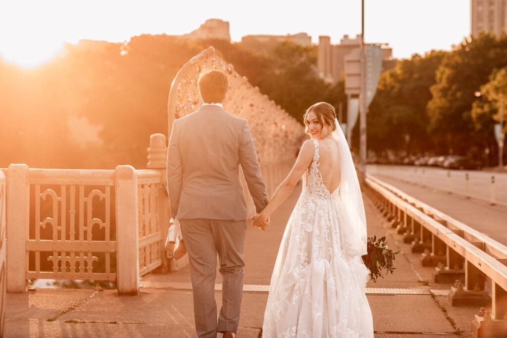 Pittsburgh bride glances back at the camera as she and her groom walk toward the Locks of Love bridge at golden hour
