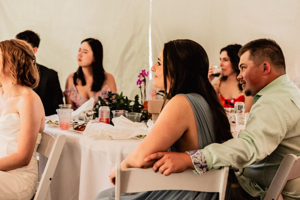 Wedding guests smiling and laughing while listening to heartfelt speeches at a Schenley Park Welcome Center microwedding reception