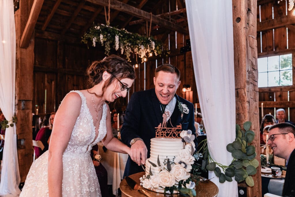 Bride and groom laughing while cutting their wedding cake at Pinehall at Eisler Farm fall wedding reception