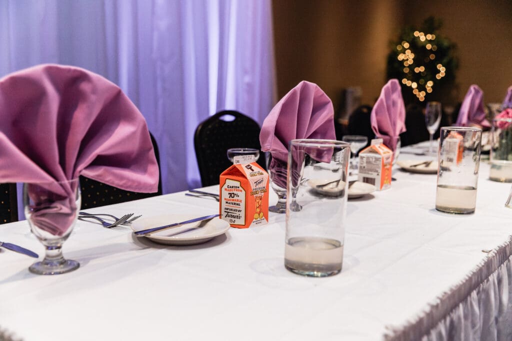 Wedding reception table setting with white linens, drinks, and purple napkins at The Fez