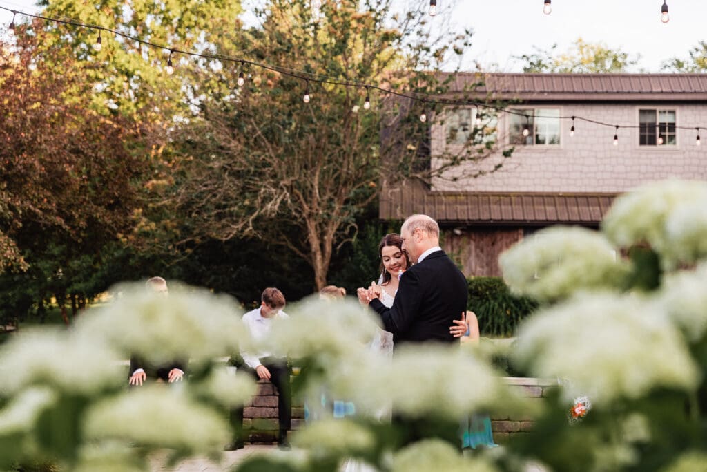 Bride and dad dances together on a stone patio at Willowbrook during their reception