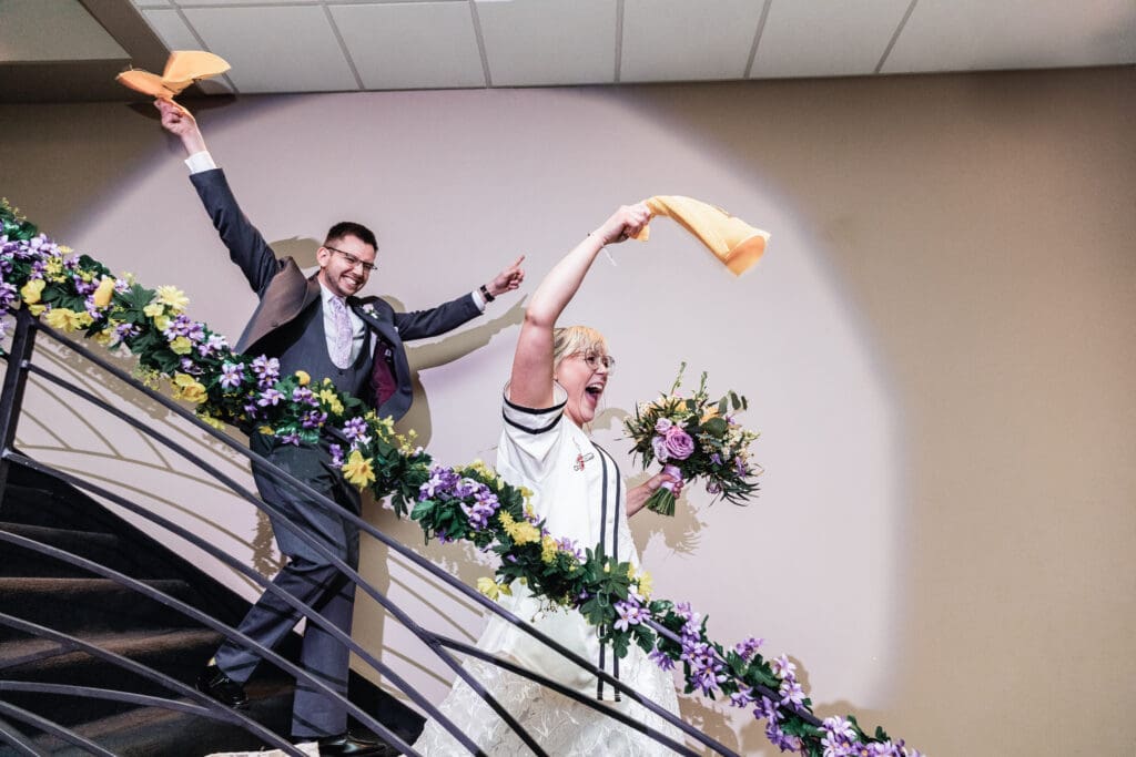 Wedding couple celebrates with raised arms while descending a floral-decorated staircase at The Fez