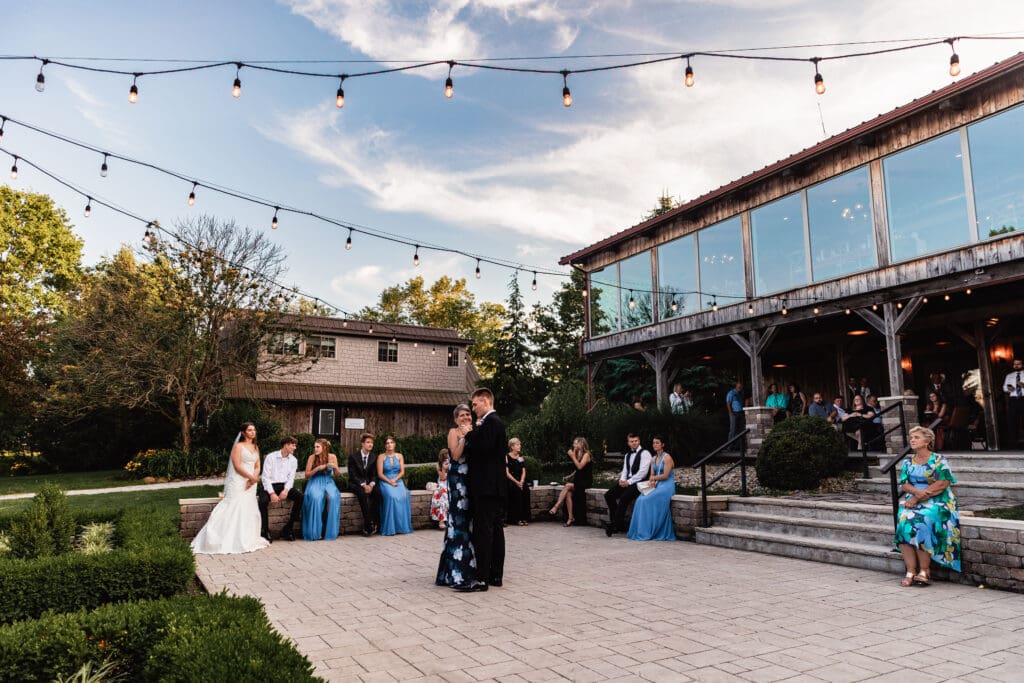 Groom and mom dances on an outdoor patio under string lights at a Willowbrook wedding