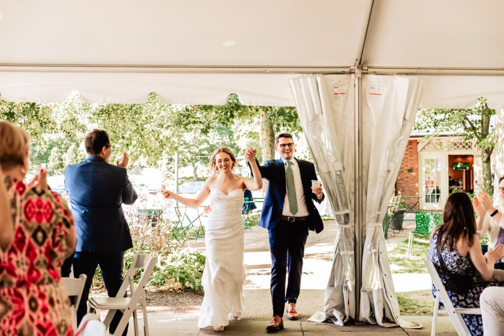 Bride and groom making their grand entrance under a white tent at their Schenley Park Welcome Center reception