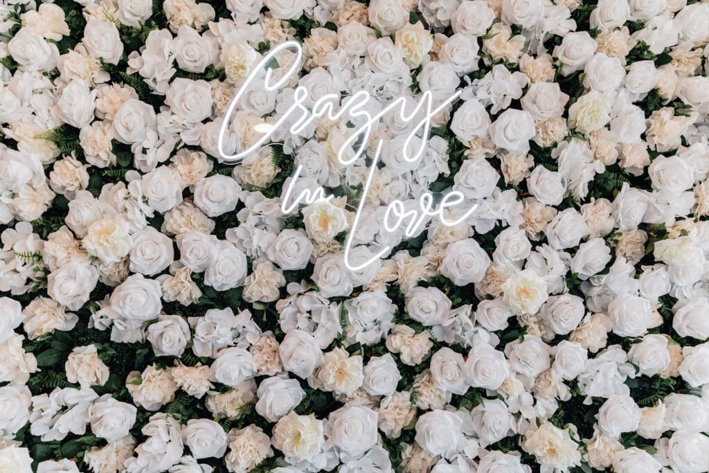 Close-up of flower wall backdrop with “Crazy in Love” neon sign at Le Mont in Mt. Washington
