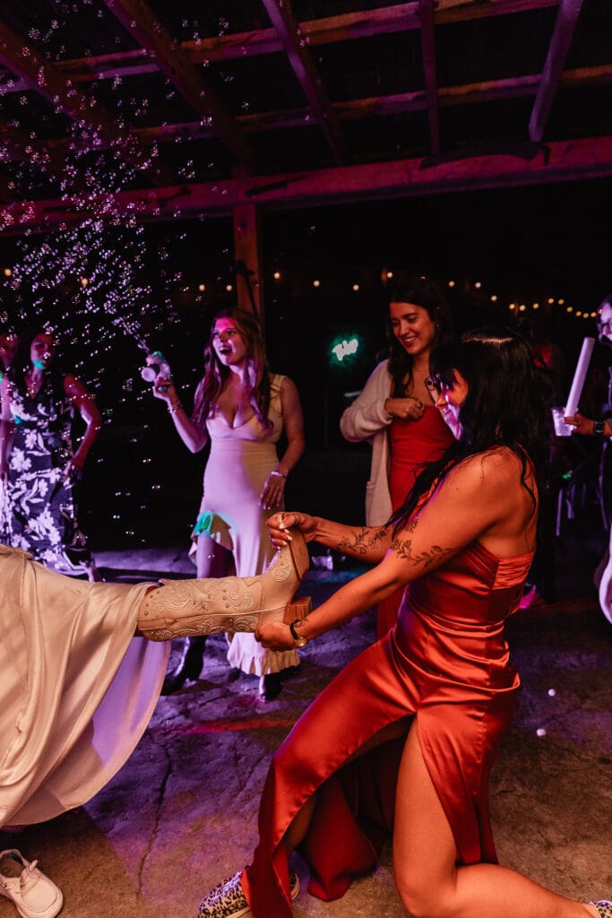 Wedding guests dancing on a rustic barn dance floor with pink and purple lighting at Hinckston Run Farm