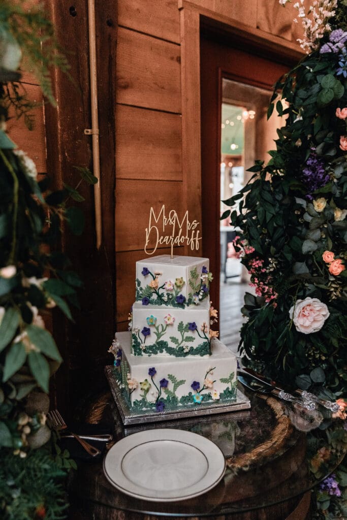 Elegant floral wedding cake with “Mr & Mrs Deardorff” topper displayed at a rustic Lingrow Farm wedding reception