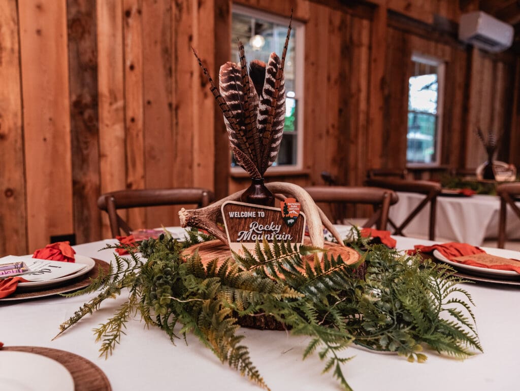 Rustic table centerpiece with feathers, greenery, and ferns on a white tablecloth at Hinckston Run Farm