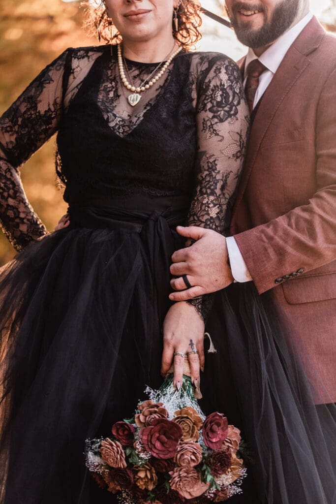 Close up of black lace, burgundy suit, dark flowers, and rings at Deep Creek wedding during sunset
