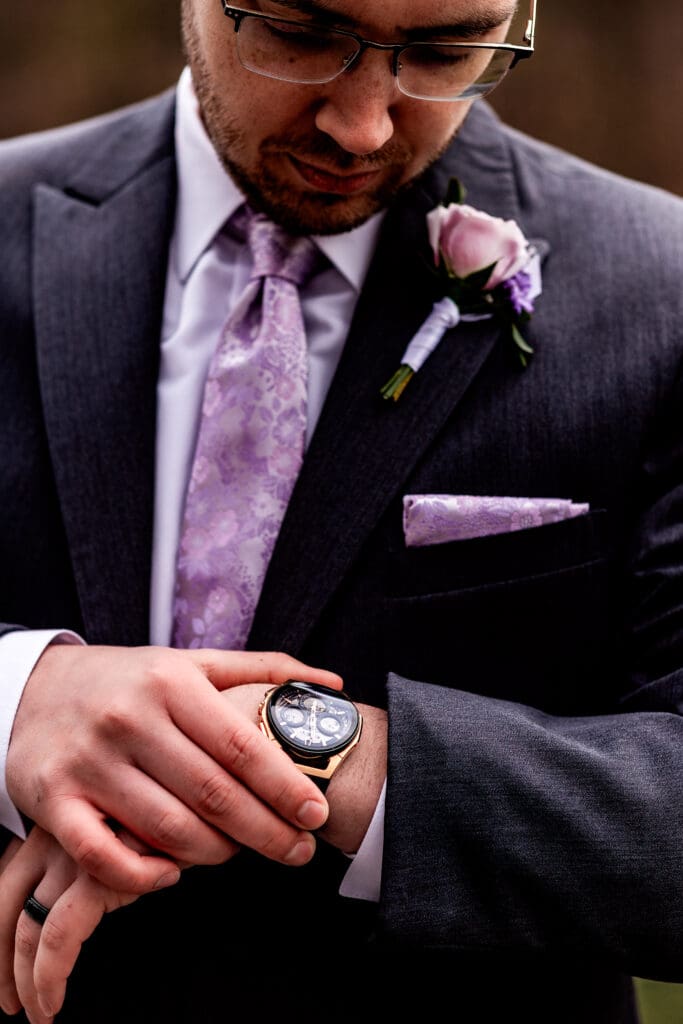 Groom in charcoal suit with purple tie checking his watch on wedding day at The Fez