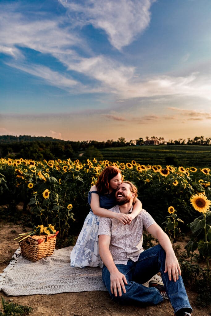 Couple snuggling on rustic blanket in sunflower field at sunset during engagement session at Schwirian Sunflower Festival