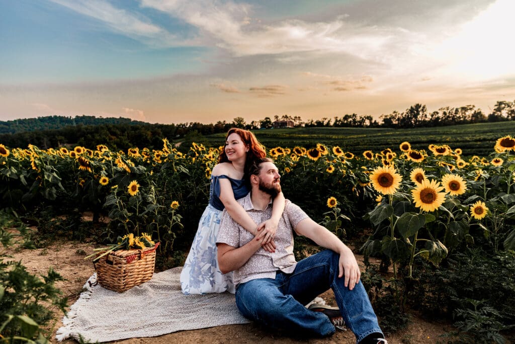 Engaged couple sitting closely together at sunset in sunflower field creating warm romantic mood at Schwirian Sunflower Festival