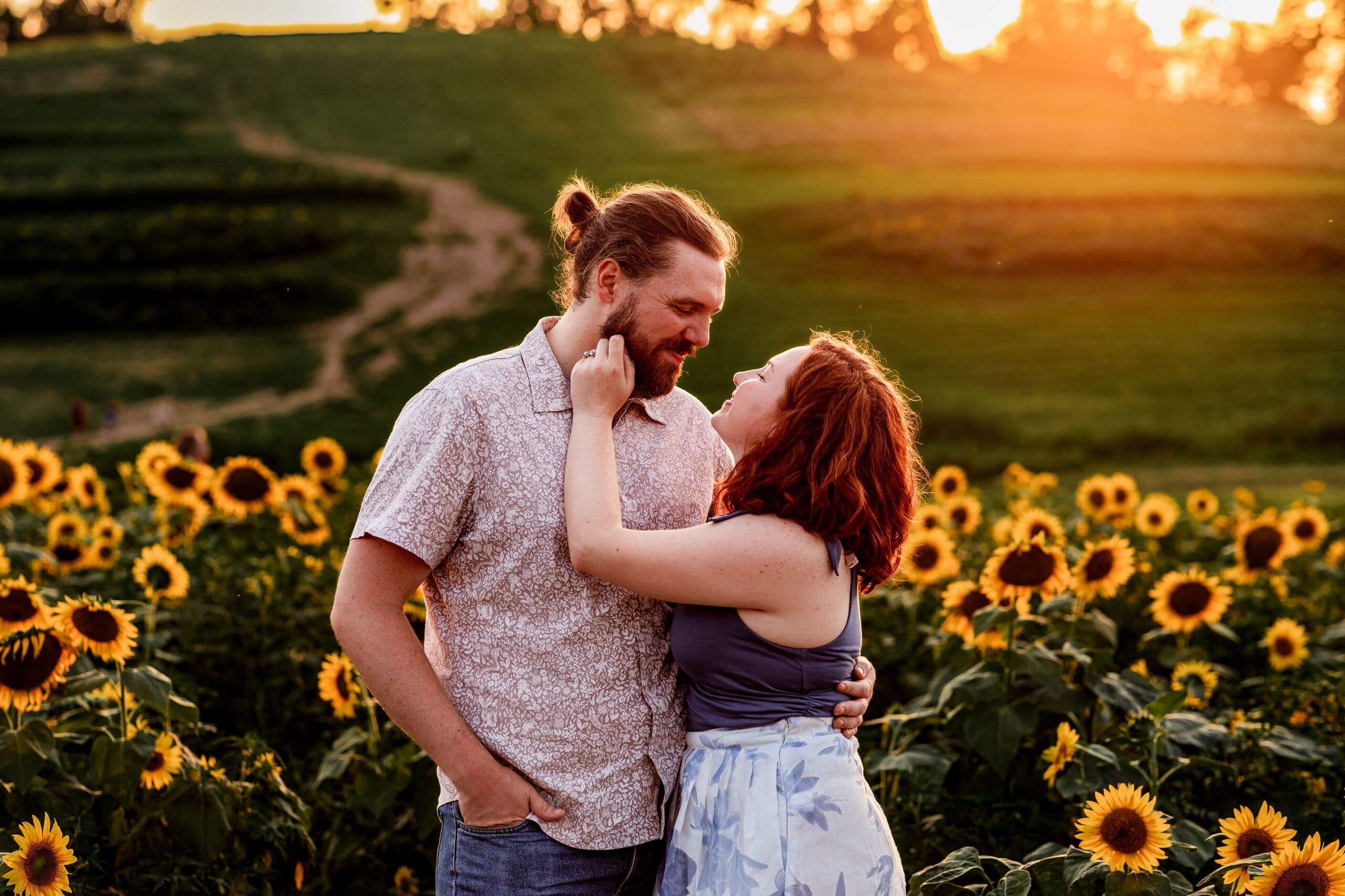 Couple sharing tender engagement moments in a sunflower field during golden sunset at Schwirian Sunflower Festival