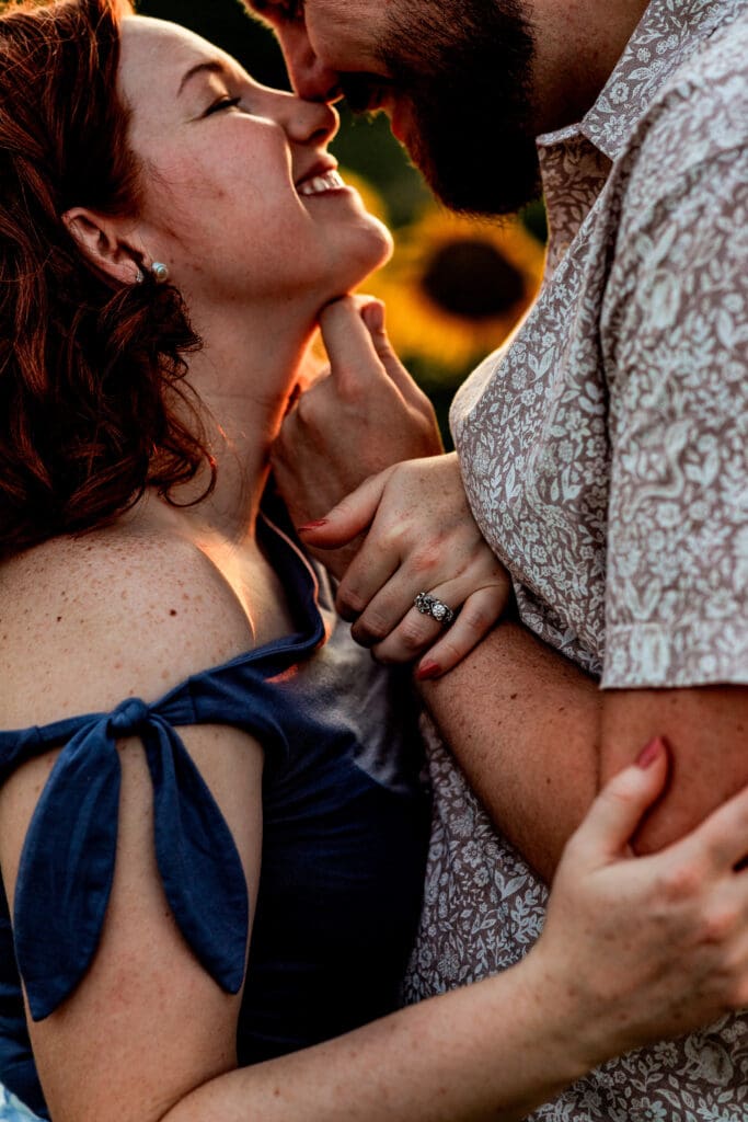 Close-up engagement photo of couple embracing in soft sunset light wearing navy blue and white at Schwirian Sunflower Festival