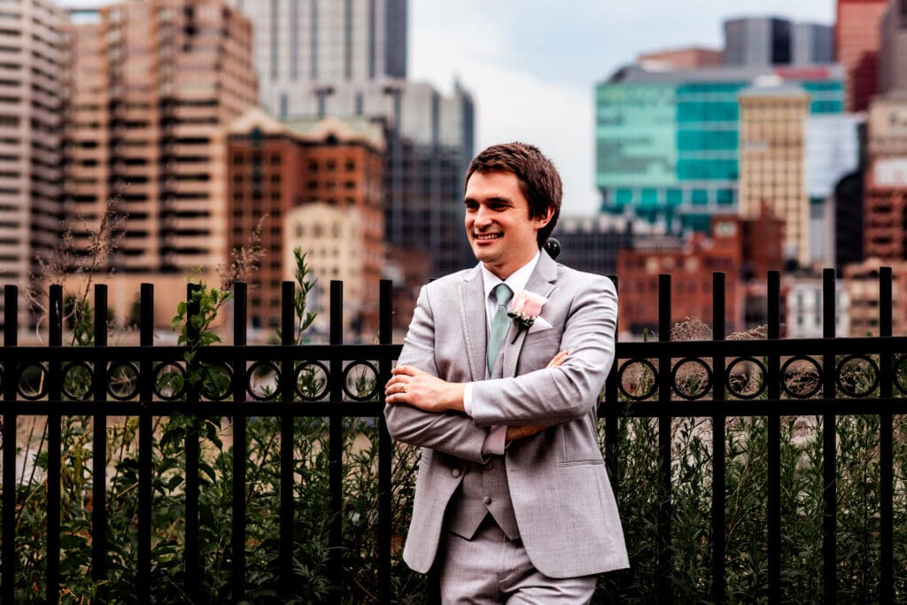 Groom leans against a fence for portraits at Sheraton Station Square