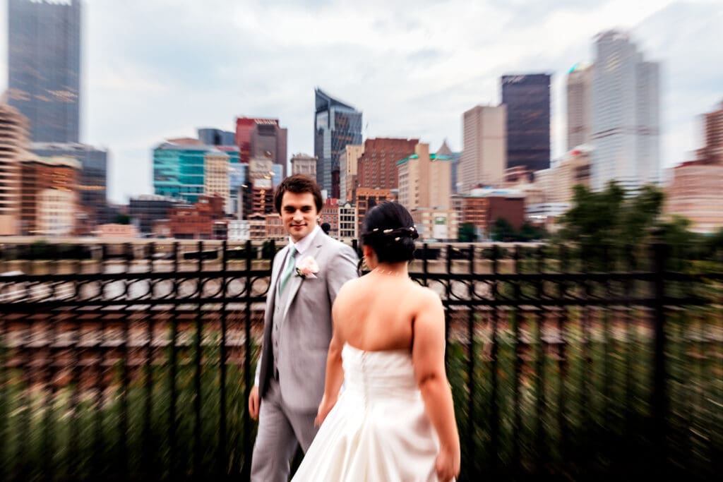 Shutter drag photo of wedding couple walking with Pittsburgh skyline behind Sheraton Station Square