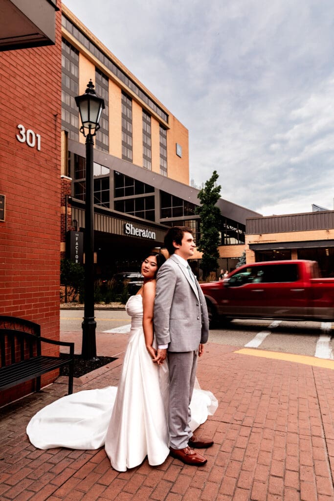 Wedding couple stands on brick pavement in front of Sheraton Station Square