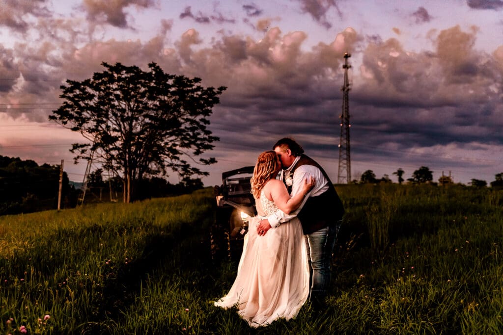 Bride and groom kissing in front of an ATV in a field at their family farm wedding in Monongahela, Pennsylvania at sunset