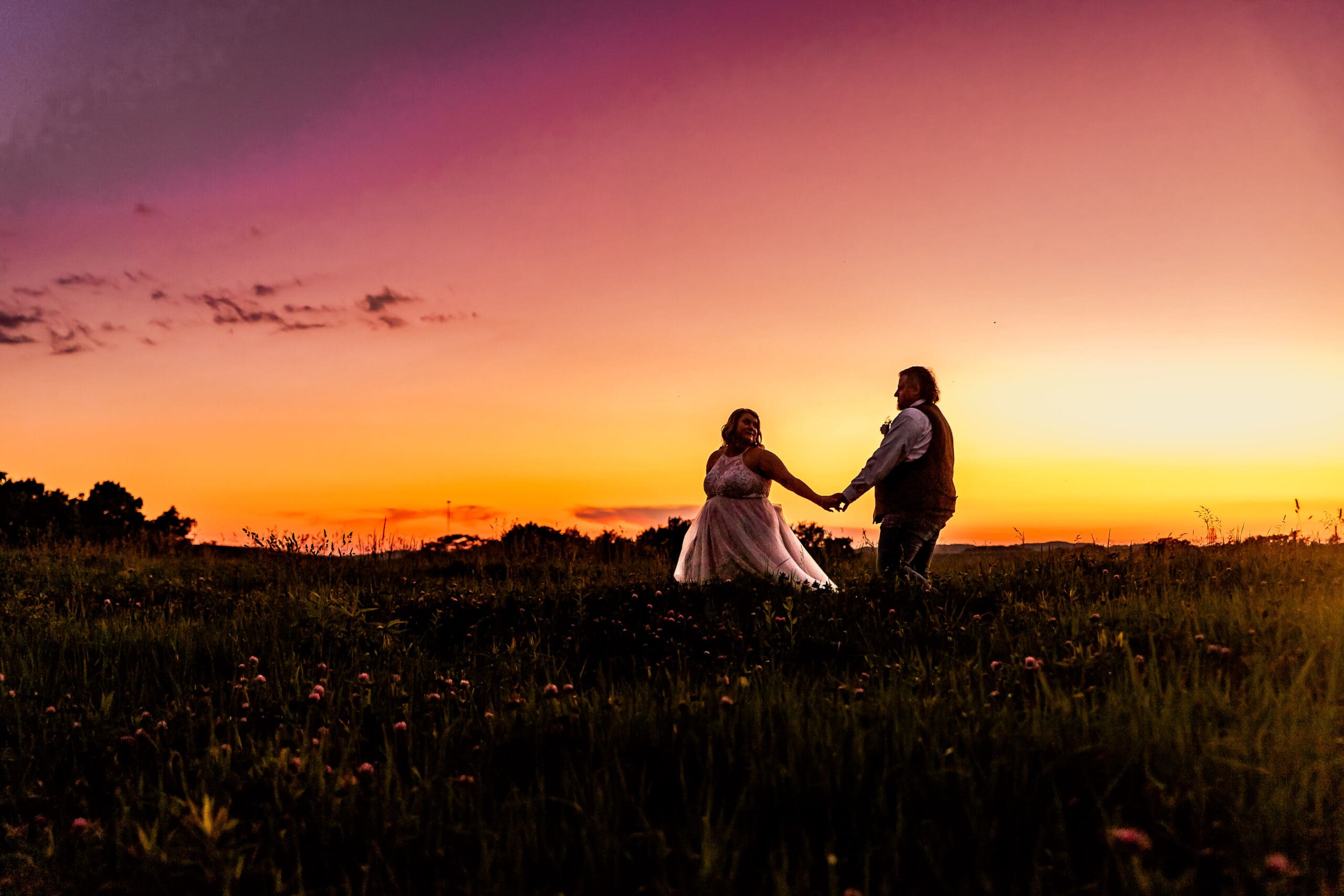 Bride and groom walking hand in hand through a field at their family farm in Monongahela, PA during sunset