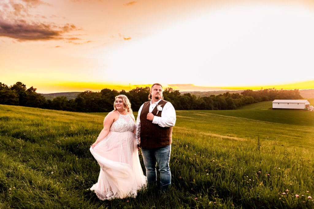 Bride and groom standing together in a field at their family farm in Monongahela, PA as the sun sets