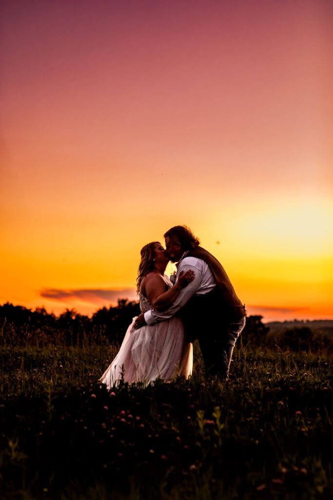 Bride and groom sharing a kiss in an open field at their family farm wedding in Monongahela, Pennsylvania at sunset