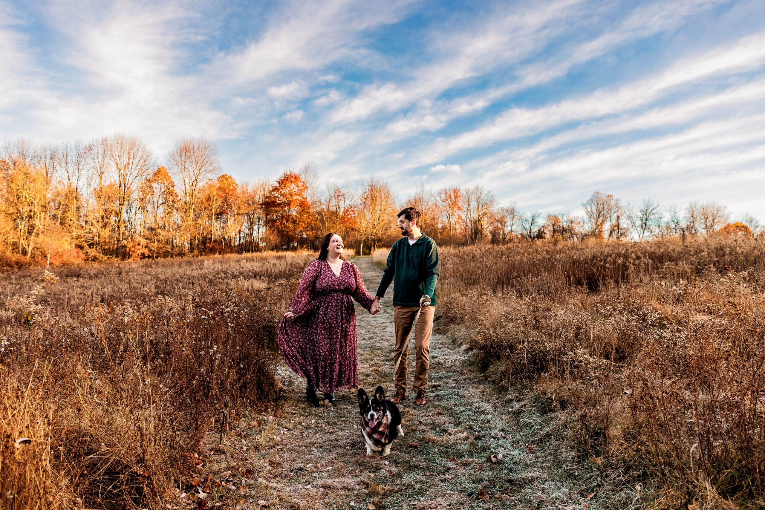 Couple walks together with their corgi through a field at Sewickley Heights Borough Park during an engagement photo session