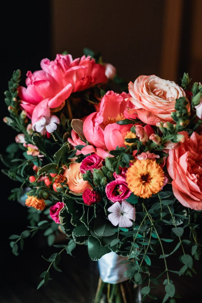 Pink and coral ranunculus and garden roses with greenery in moody lighting at National Aviary wedding