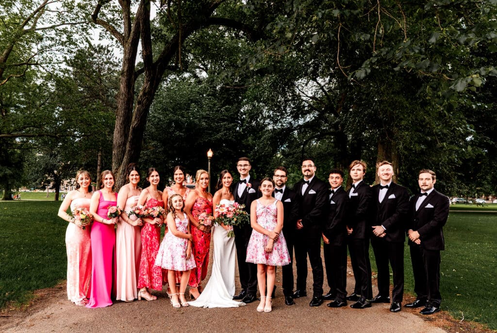 Wedding party in pink dresses and black suits posing along tree-lined garden path at the National Aviary