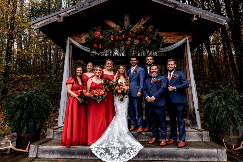 Wedding party in terracotta dresses and navy suits poses under rustic wooden gazebo at Hinckston Run Farm
