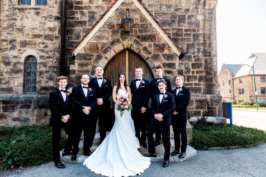 Bride poses with groomsmen in black suits at a Willowbrook wedding
