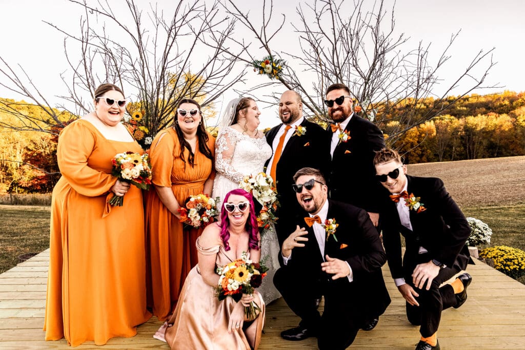 Wedding party wearing heart-shaped sunglasses crowding around bride and groom and laughing at fall Ridgemont Farm wedding
