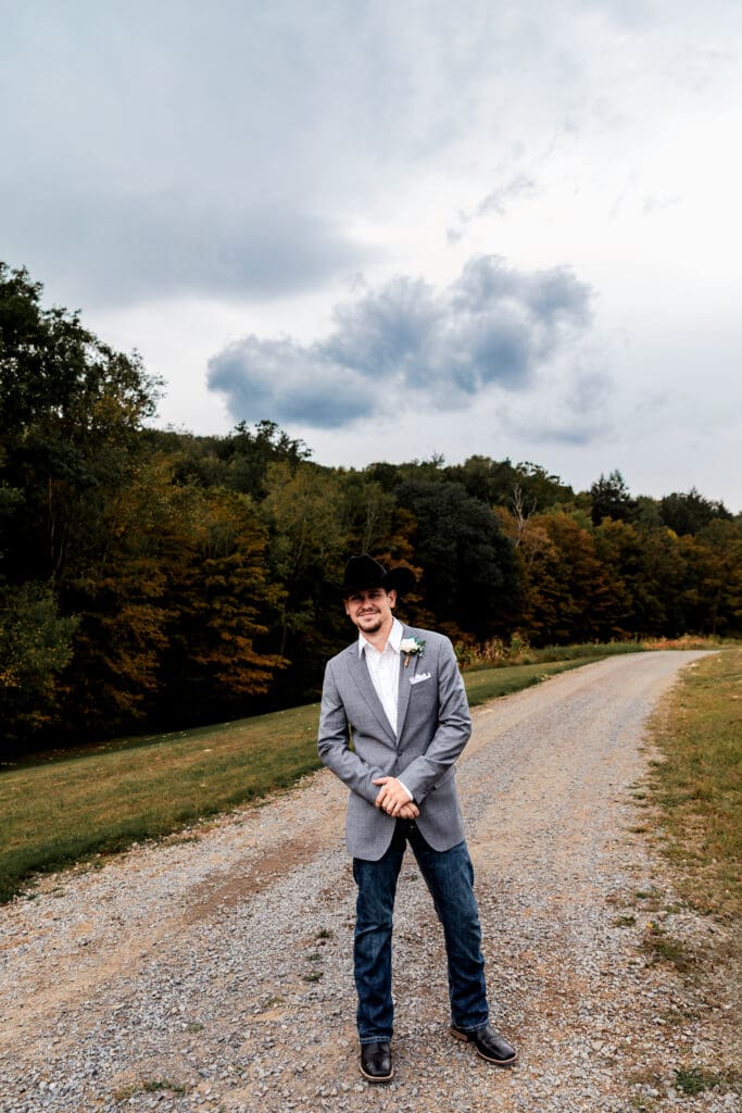 Groom posing on gravel path surrounded by fall trees at Hinckston Run Farm