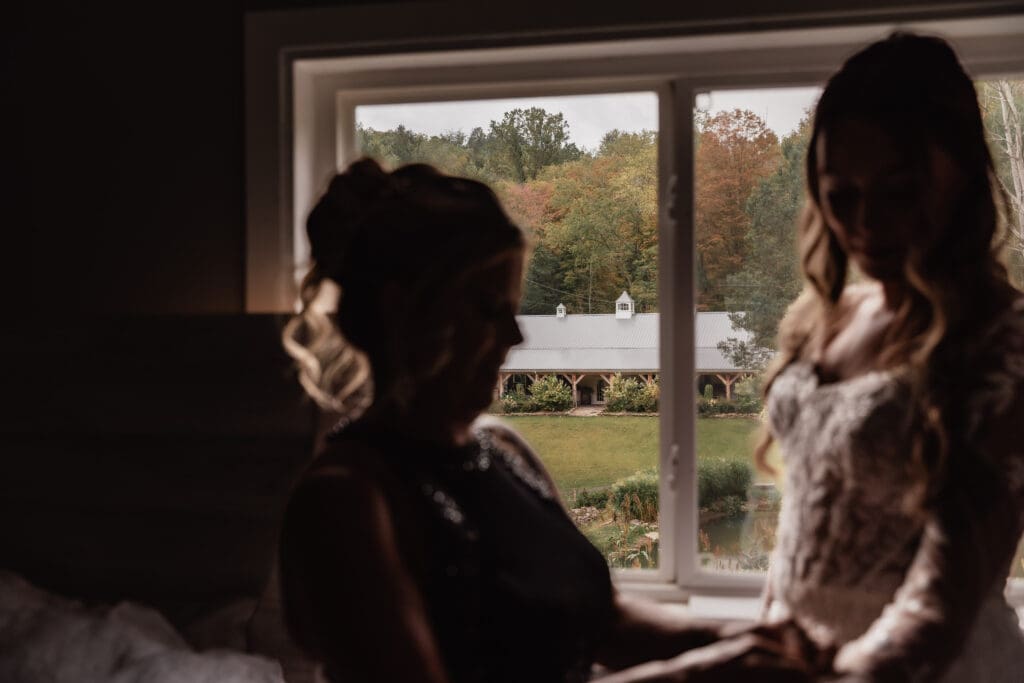 Silhouette of mother and bride with wedding reception venue visible through window at Hinckston Run Farm