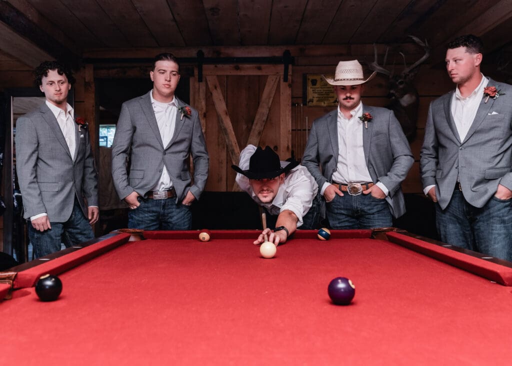Groom and groomsmen gathered around pool table during wedding celebration at Hinckston Run Farm