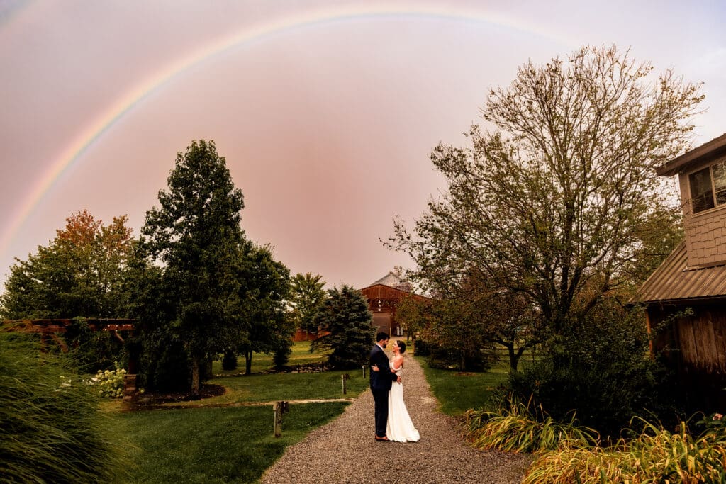 Bride and groom embracing beneath a dramatic rainbow at Willowbrook wedding reception in Volant, PA