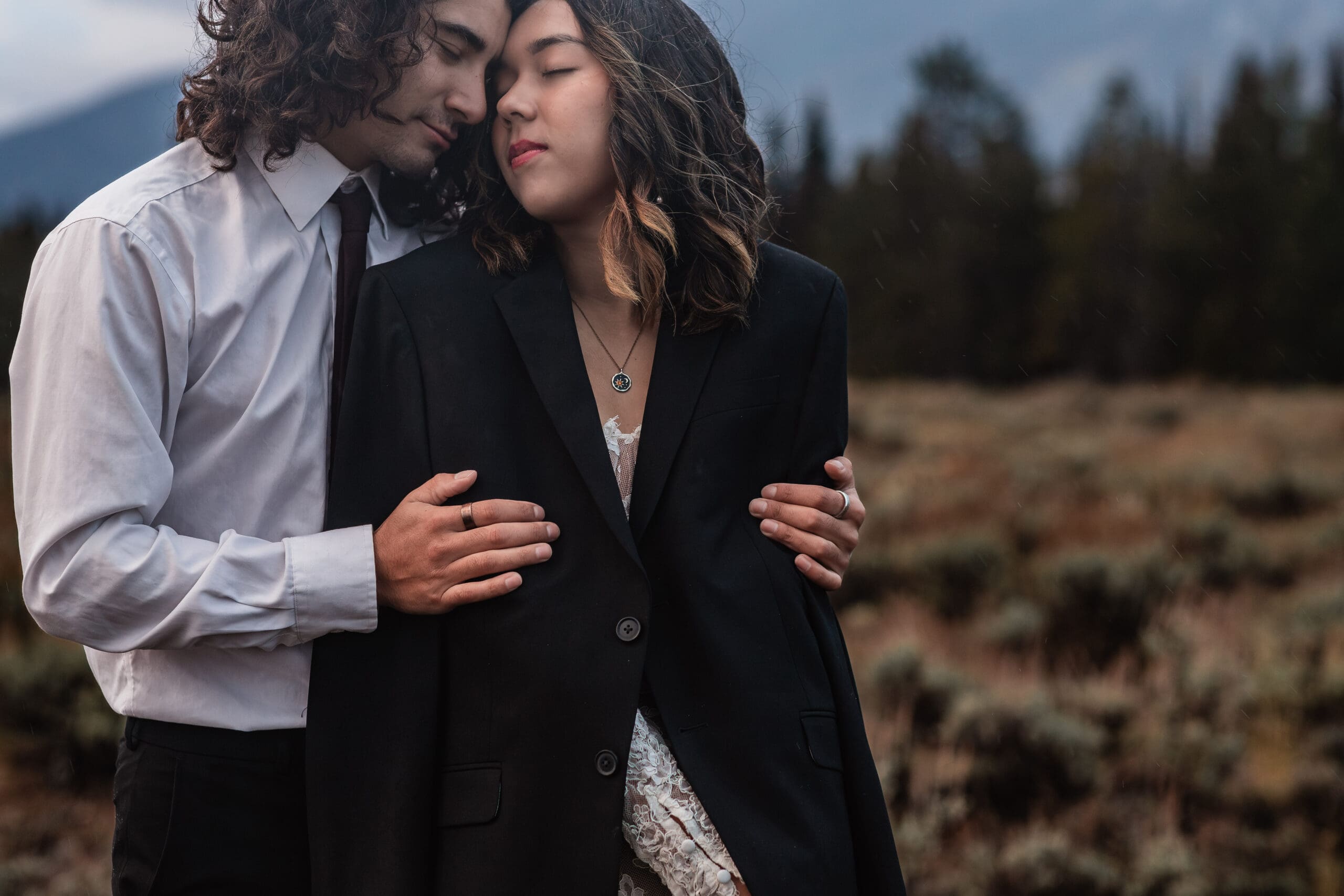Close-up of an eloping couple’s hands wrapped together while they snuggle in front of the Teton mountains.
