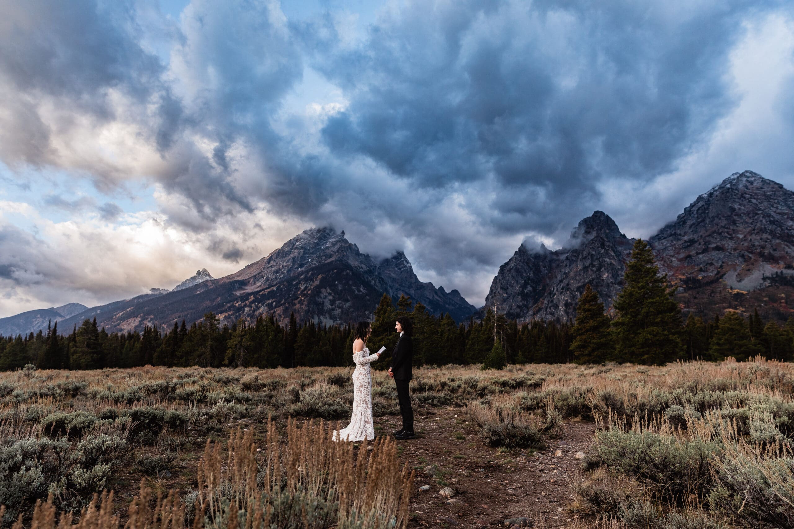 Couple standing together while sharing heartfelt vows with the Teton mountain range rising behind them in Grand Teton National Park.