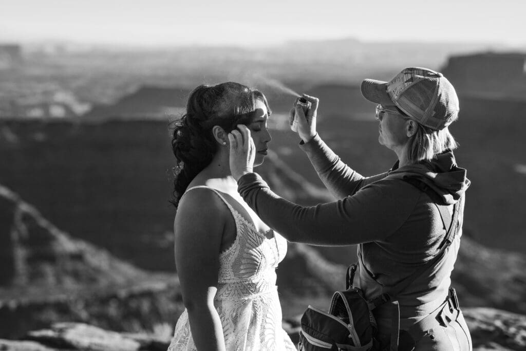 Hair stylist and makeup artist putting the finishing touches on the bride’s hair and makeup at Marlboro Point during a Moab adventure elopement.