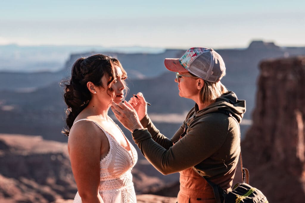 Bride smiling as her hair and makeup are adjusted by her beauty team during a scenic getting ready moment at Marlboro Point in Moab.