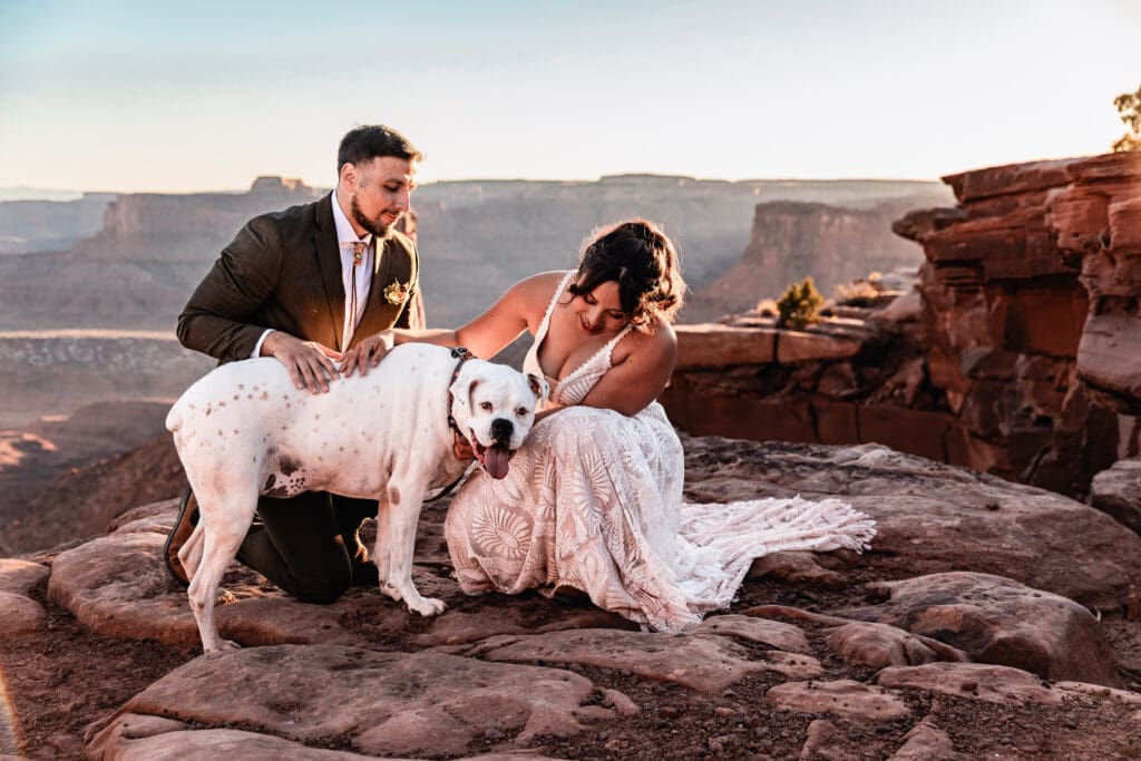 Just-married couple celebrating and loving on their dog after their intimate elopement ceremony on BLM land in the red rock desert of Moab, Utah.