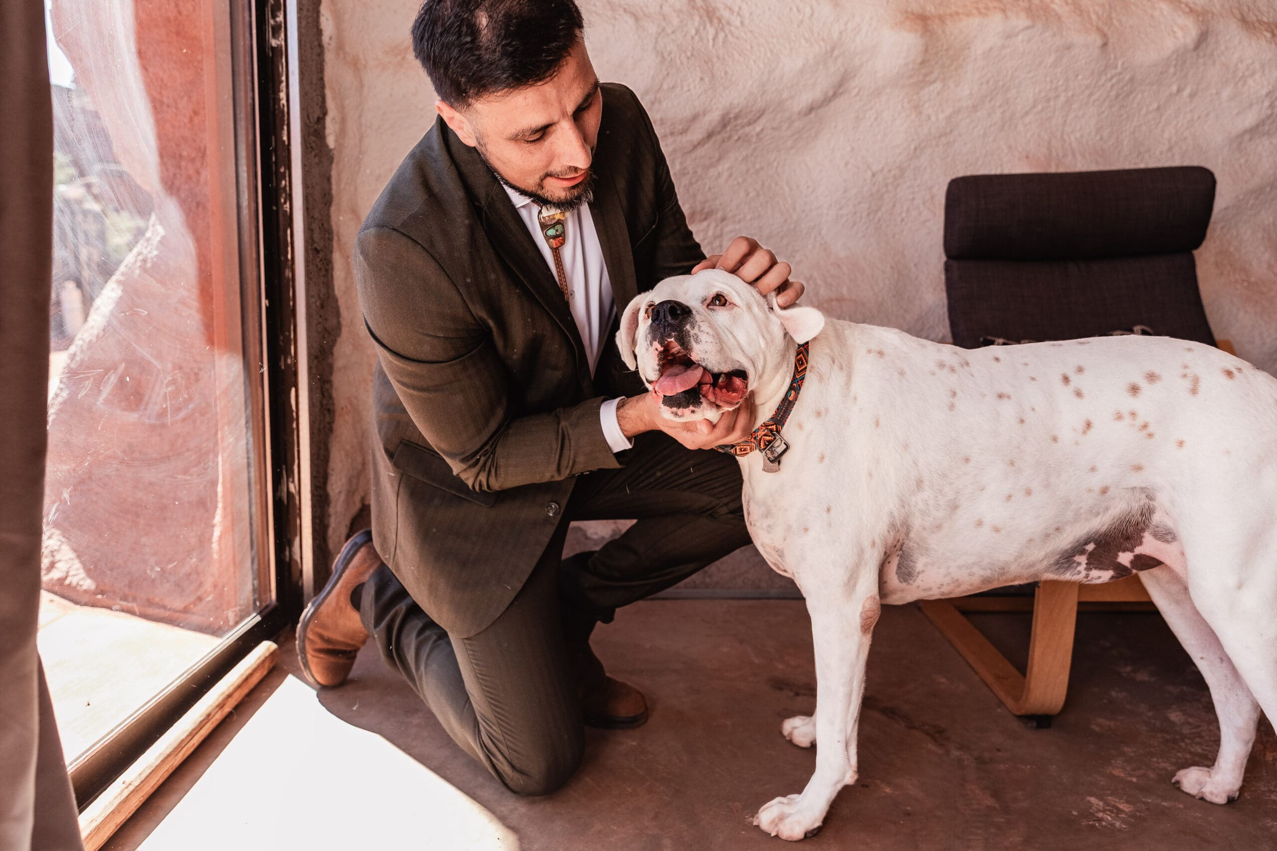 Groom kneeling down to hug and love on his dog while getting ready for a relaxed dog-friendly elopement in Moab.