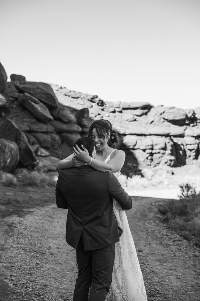Groom lifting and spinning his bride in celebration on a dusty canyon road during their Moab adventure elopement.