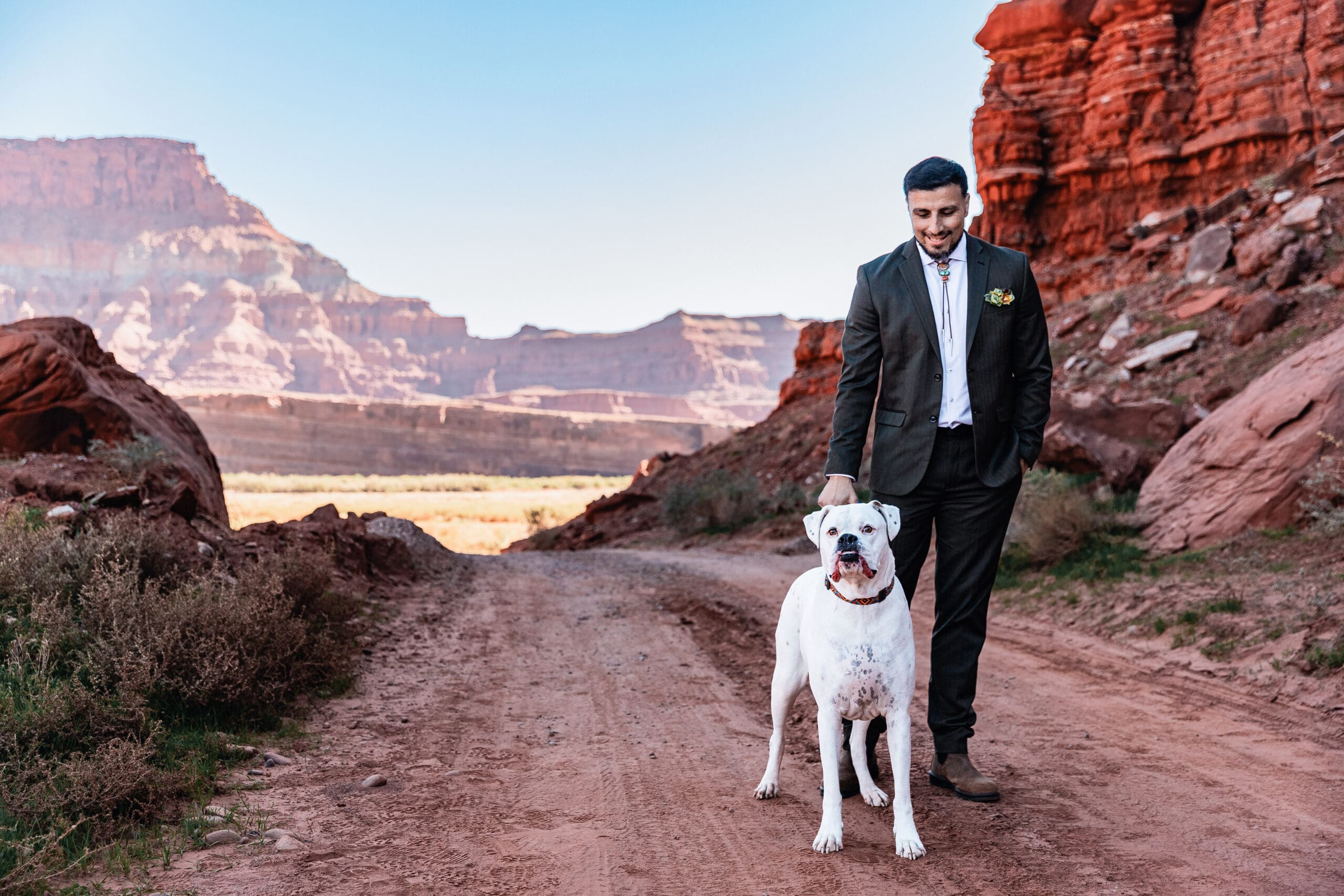 Groom walking with his dog through the red rock desert landscape during their adventurous dog-friendly Moab elopement.