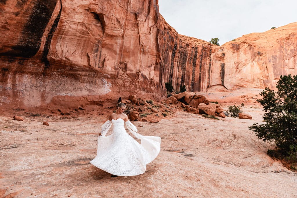 Bride twirling in her wedding dress along the Corona Arch trail surrounded by the red rock desert near Moab.