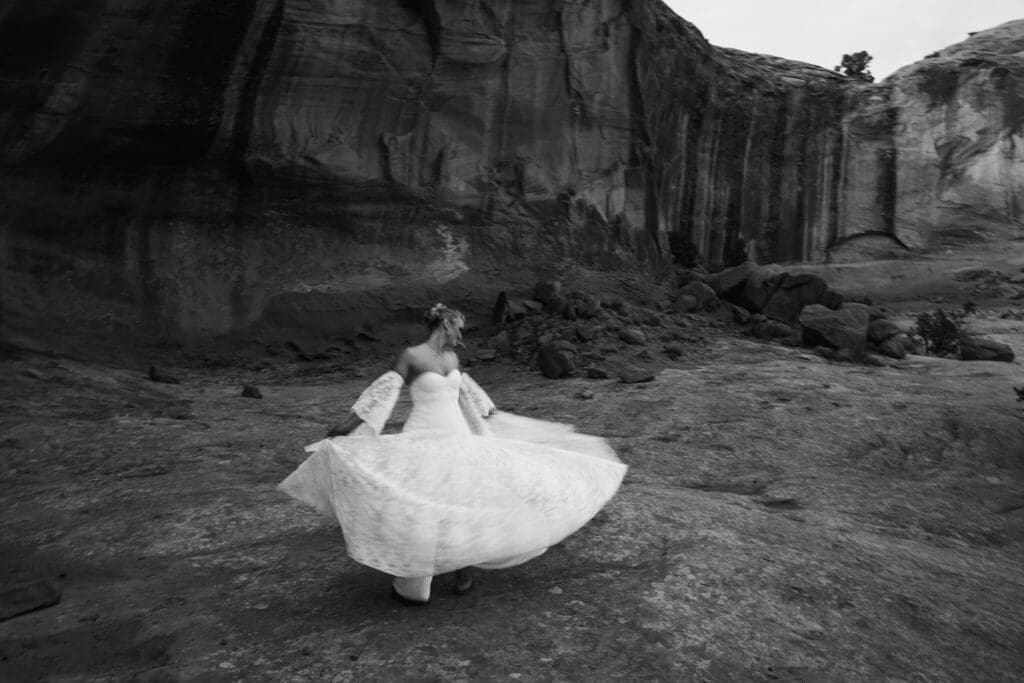 Black and white motion blur photo of the bride spinning in her wedding dress before exchanging vows at Corona Arch during a Moab elopement.