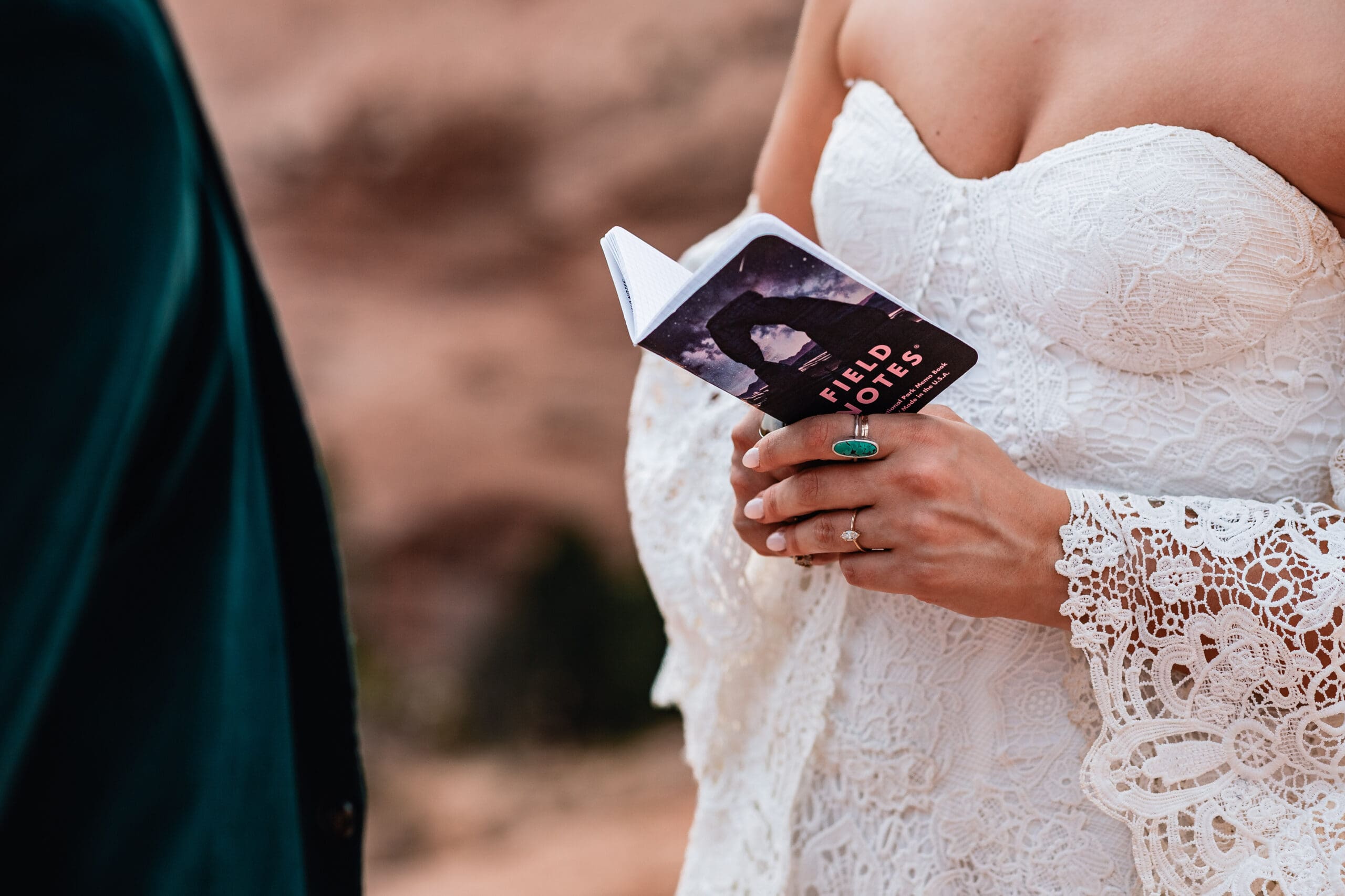 Close-up of a bride’s hands holding her vow book while reading personal vows during an intimate elopement ceremony at Corona Arch near Moab, Utah.